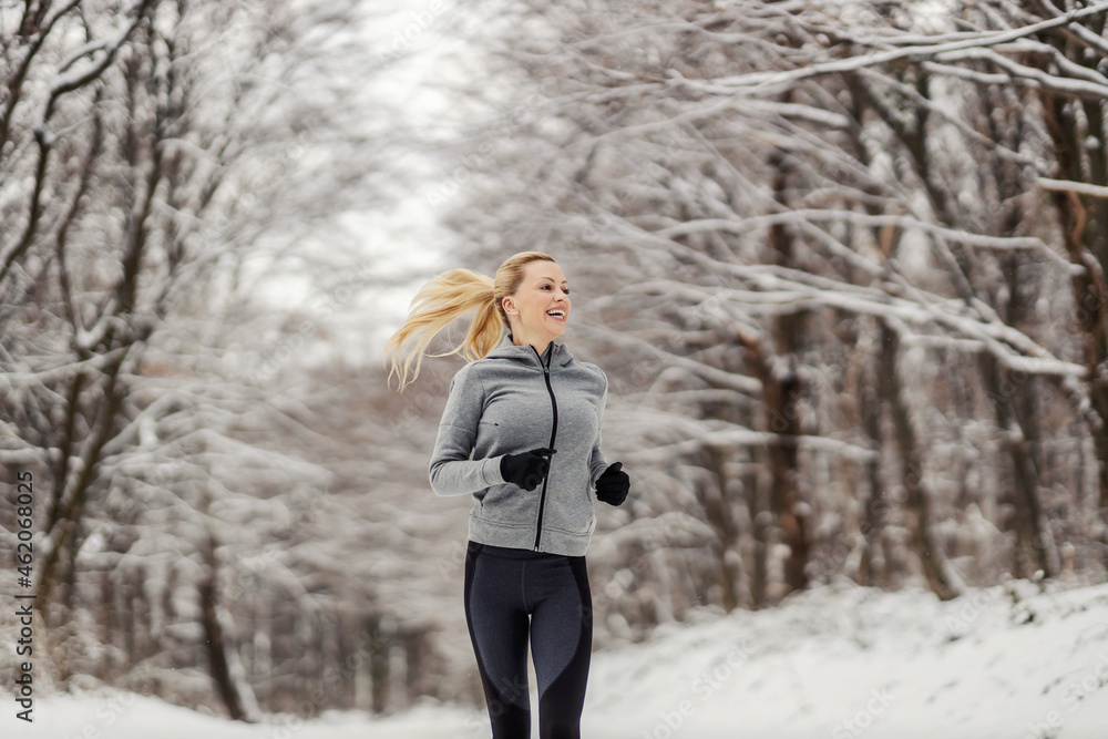 Happy fit sportswoman jogging in woods at snowy winter day. Outdoor fitness, winter fitness, healthy lifestyle