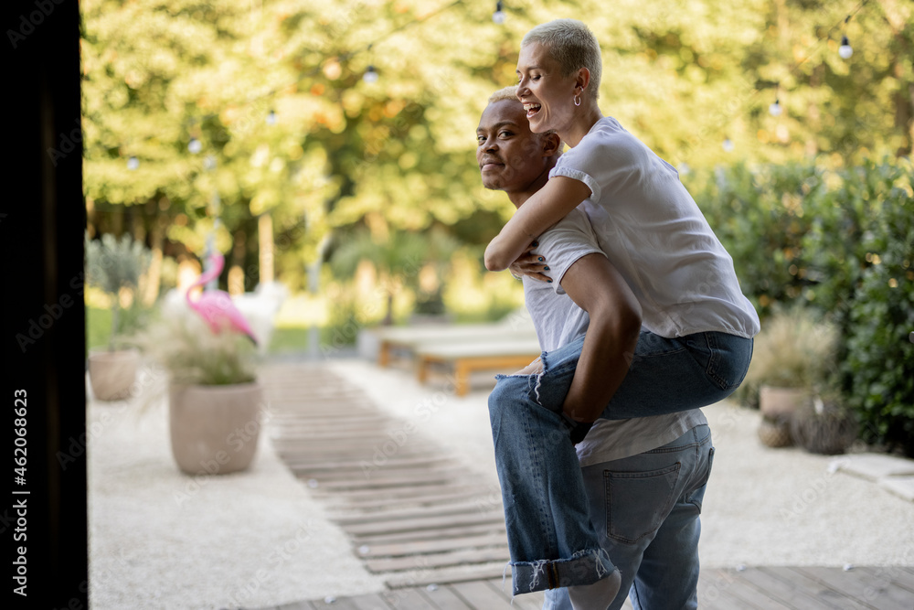 Latin boyfriend giving piggyback ride for his caucasian girlfriend on home terrace. Concept of relationship and enjoying time together. Modern domestic lifestyle. Warm sunny daytime. Latin boyfriend giving piggyback ride for his caucasian girlfriend on home terrace. Concept of relationship and enjoying time together. Modern domestic lifestyle. Warm sunny daytime.