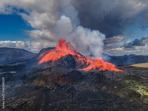 Aerial view of the crater opening from Fagradalsfjall volcano. Crater with strong lava flow on Iceland in the GeoPark. Daytime volcanic eruption on Reykjanes peninsula. Clouds and steam in the sky