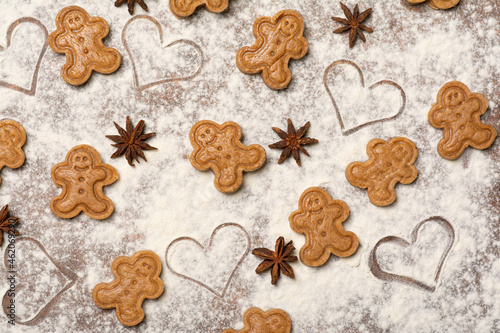 A colourful happy pattern made of unbaked gingerbread man cookies, star anise fruits and seeds and heart-shaped marks on the kitchen worktop sprinkled with flour. 