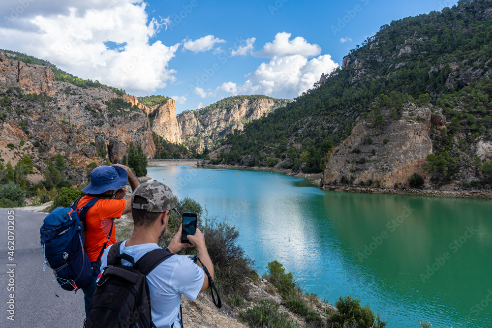 Two unrecognizable hikers taking photos of a reservoir and a mountainous landscape, in Villa de Ves, Albacete (Spain).