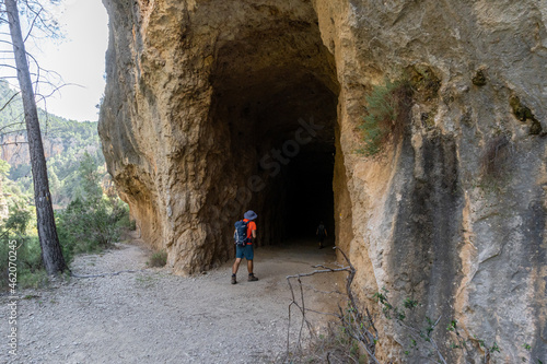 Hiker man seen from behind entering a tunnel dug into the rock of the mountain.