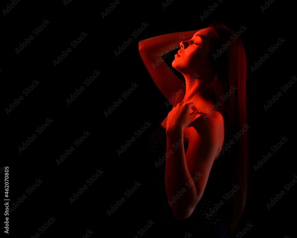 portrait of a beautiful young woman with closed eyes and bare shoulders, isolated on black background with red light