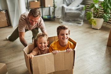 Portrait of happy father playing with two sons in cardboard box while family moving to new house, copy space