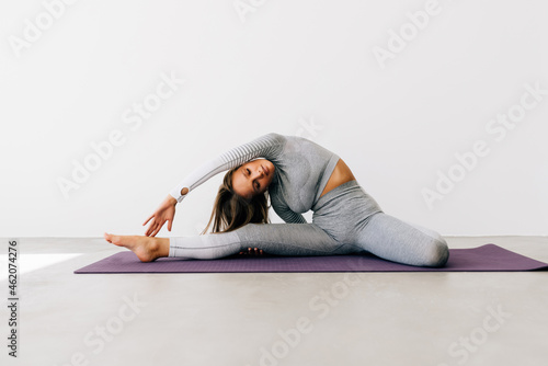 A young slender woman does splits to stretch her legs. Joyful talented woman doing twine in studio. Healthy lifestyle, sport concept.
