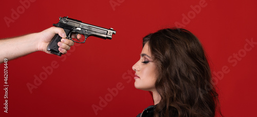 Hand with a pistol aimed at a girl on red background