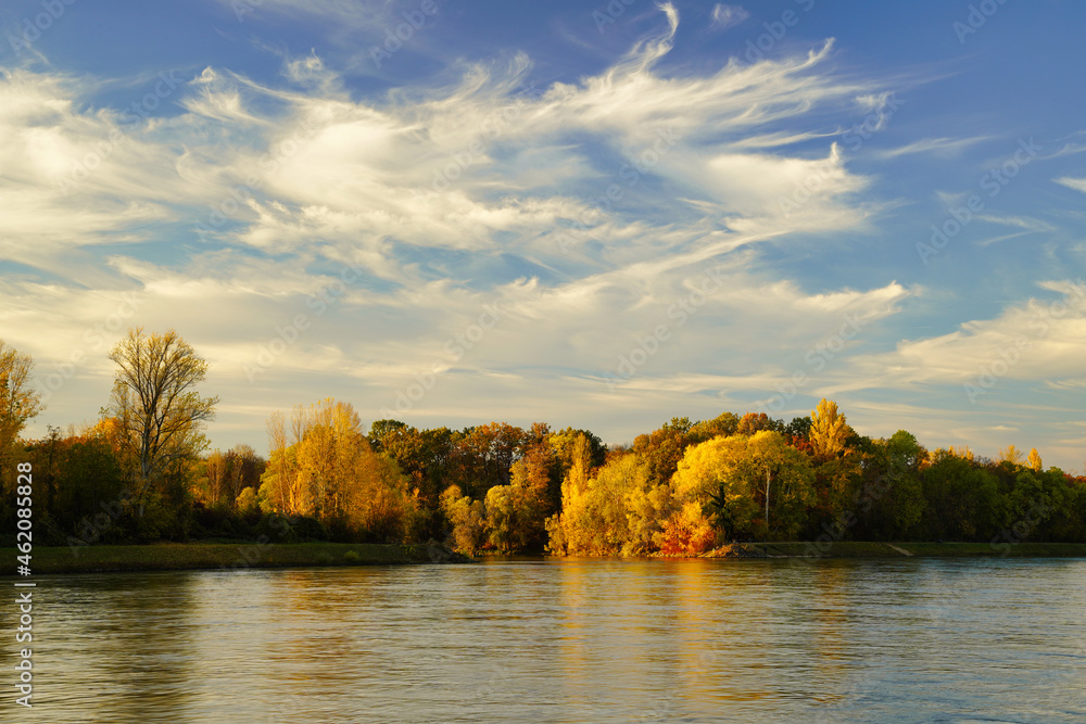 A beautiful autumn evening at river Rhine. Bright colorful trees on the other side of the river. Germany, Baden-Wuerttemberg.