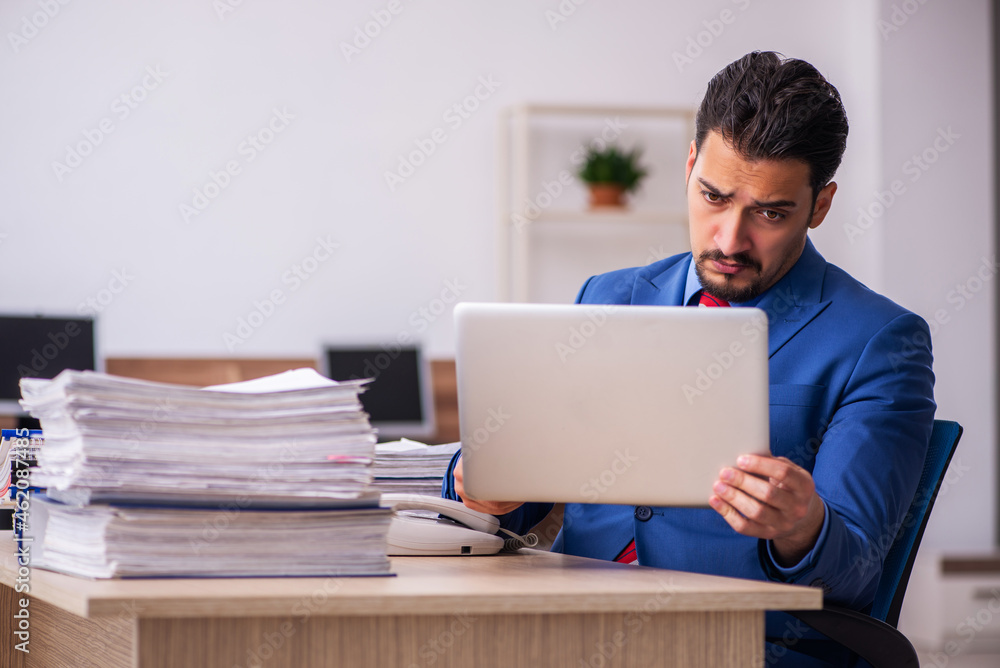Young male employee unhappy with excessive work at workplace Young male employee unhappy with excessive work at workplace