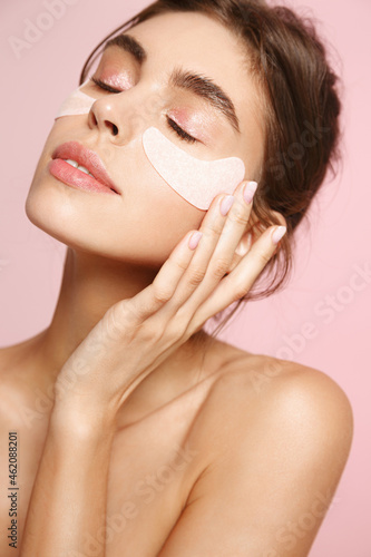 Skin care and cosmetology. Beautiful natural woman with healthy skin, applying under eye patches from puffiness and dark circles, pink background