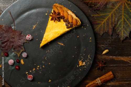 The last piece of pumpkin pie on a black plate. Flatlay on a dark wooden background with bright autumn leaves.