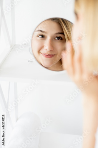 Beauty freshness. Female dermatology. Skin health. Cheerful woman touching gorgeous radiant face at mirror reflection in light free space.