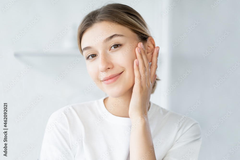 Beauty model. Skincare treatment. Facial care. Gorgeous fresh young woman touching perfect radiant face skin on defocused light bathroom. Beauty model. Skincare treatment. Facial care. Gorgeous fresh young woman touching perfect radiant face skin on defocused light bathroom.