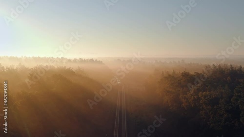 Aerial view of electric passenger train passing through the autumn foggy forest at sunny morning.