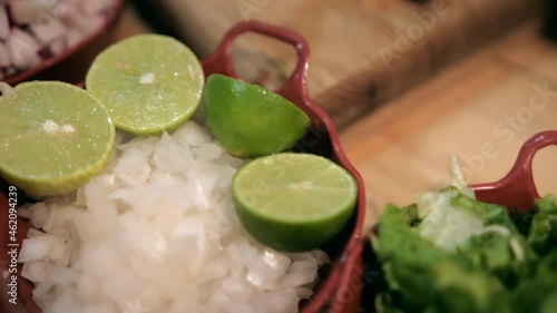 Clay pots of lettuce, chopped radishes, onions, and limes on wooden table