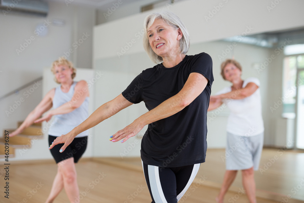 Portrait of mature energetic woman and people practicing active modern dancing in the studio at a group lesson