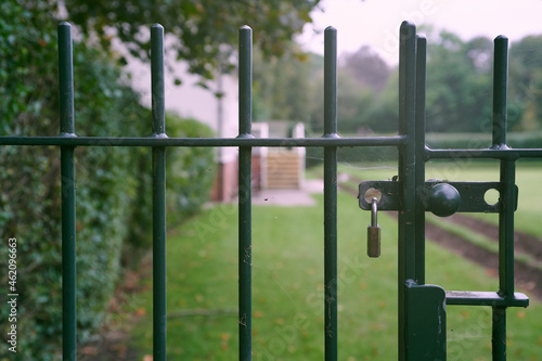 Padlocked closed green metal gate with out of focus park and lawn in background