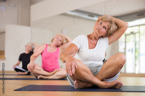 Mature active women practicing yoga in a fitness studio perform an exercise in the lotus position, holding their head with ..their hand