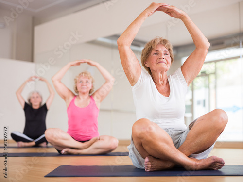 Mature women in sportswear exercising lotus pose together during group yoga class.