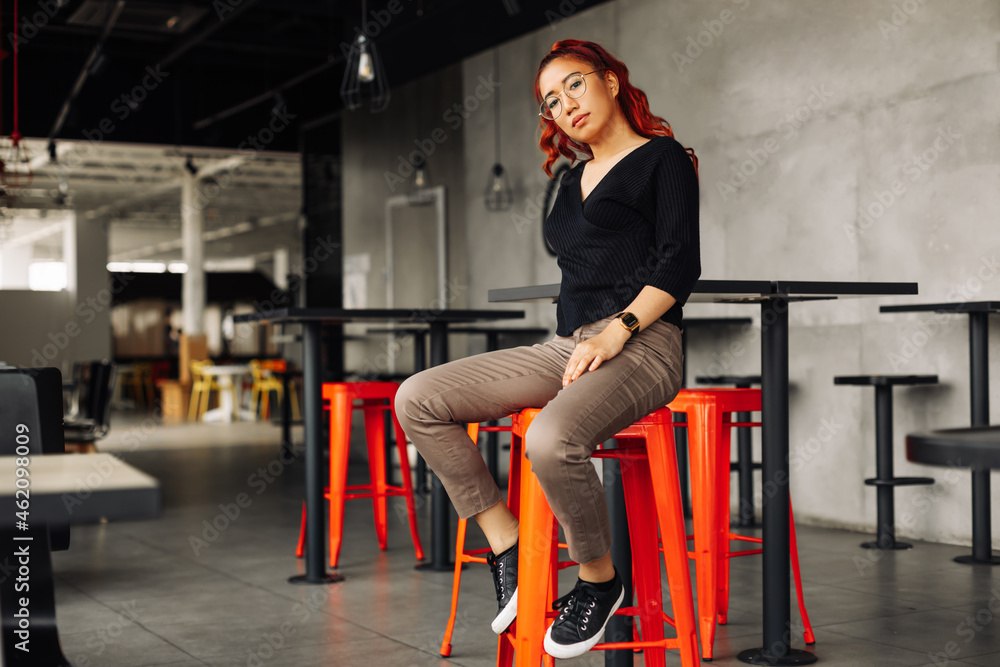 Obraz premium fashionable asian woman , posing smiling looking at the camera, happy asian woman smiling and posing in a loft cafe