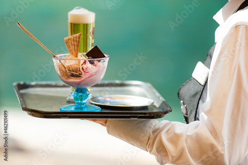 Waiter carrying the tray with ice cream and a beer