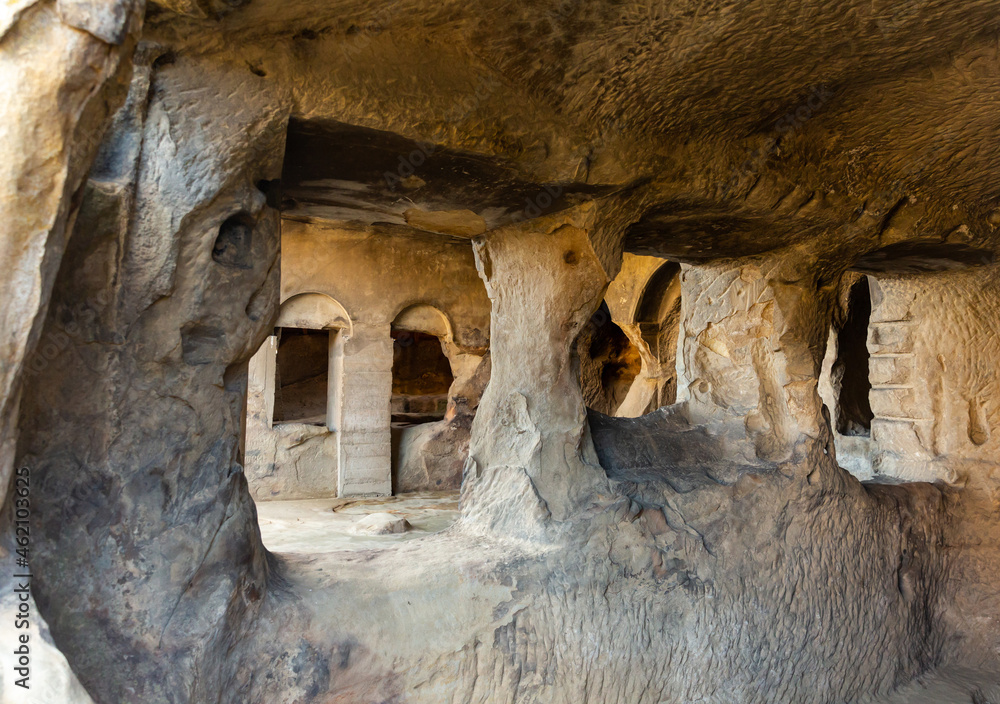 Interior of cave halls carved into mountain with pillars supporting ceiling in historical rock-hewn city of Uplistsikhe in Georgia.