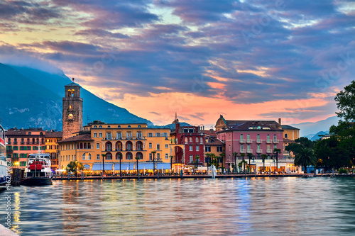 View of the beautiful Riva del Garda town at sunset with a red sky, Lake Garda surrounded by mountains in the summer, Italy