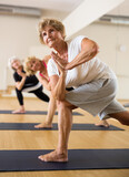 Mature women practicing yoga perform the exercise in the twisted side angle pose at a group lesson
