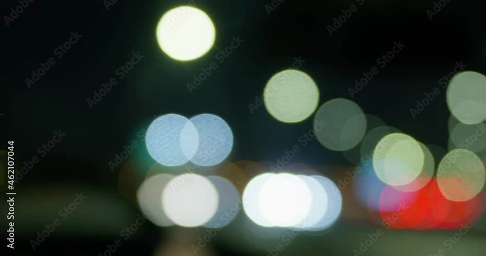 Blurred view of person driving automobile along road ON dark city street against colorful lights with bokeh effect close view Blurred view of person driving automobile along road ON dark city street against colorful lights with bokeh effect close view
