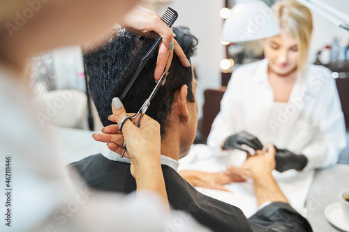 Hairdresser cutting hair of customer during manicure