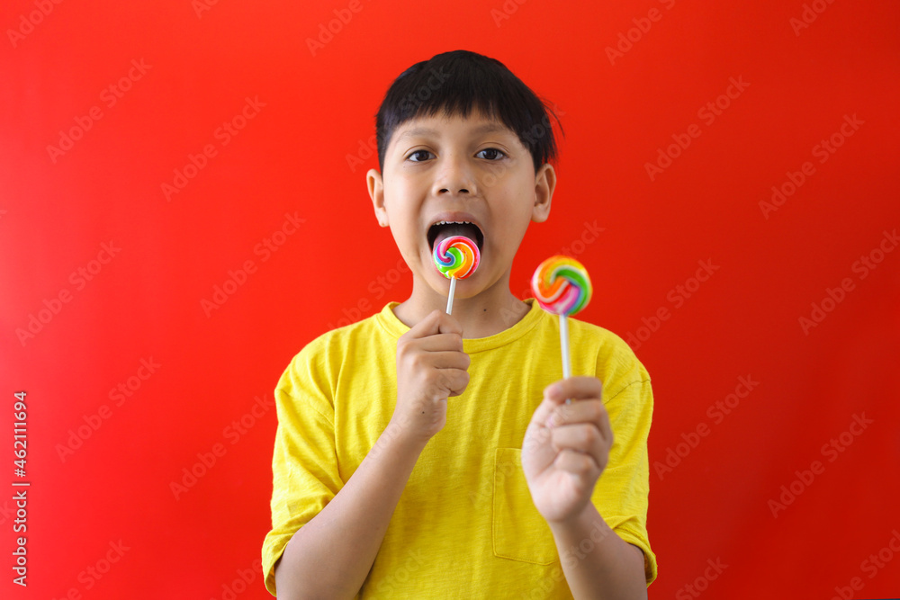 Asian boy eating lollipop candy on red background Asian boy eating lollipop candy on red background