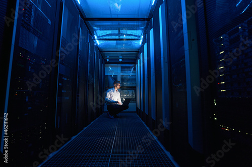 Fototapeta Naklejka Na Ścianę i Meble -  Technician looking at server cabinet while using laptop