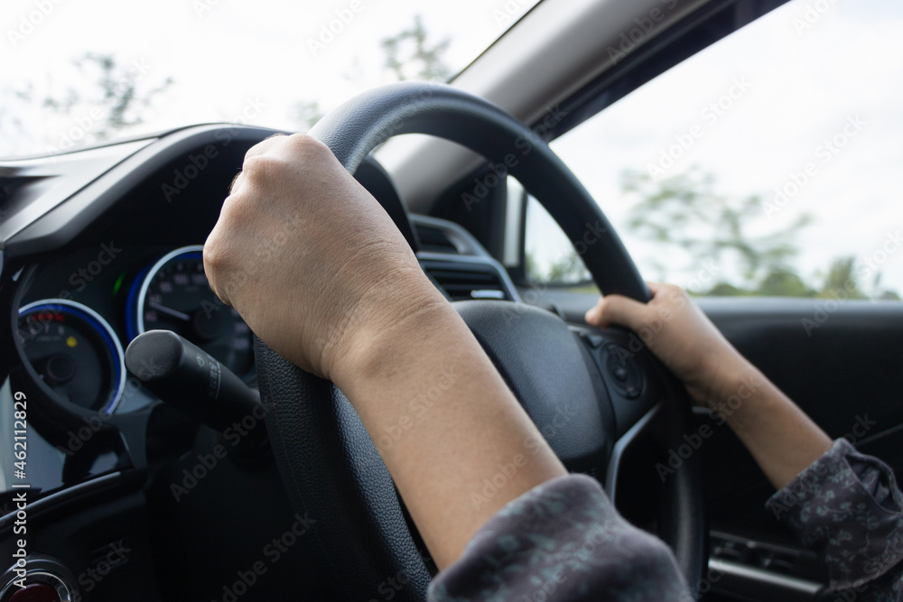 Young woman's hand is holding the black steering wheel of a car.