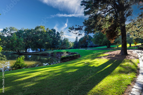 a gorgeous shot of the still waters of a lake surrounded by lush green and autumn colored trees with green grass, blue sky and clouds at Lenox Park in Brookhaven Georgia USA photo