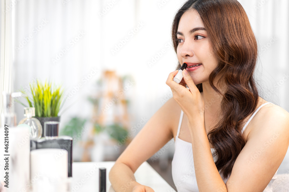 Smiling beautiful asian woman fresh healthy skin looking on mirror and enjoying applying lips with red lipstick at home.facial beauty and cosmetic concept Smiling beautiful asian woman fresh healthy skin looking on mirror and enjoying applying lips with red lipstick at home.facial beauty and cosmetic concept