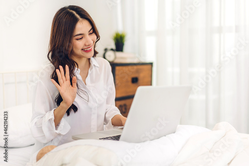 Young smiling happy beautiful asian woman relaxing using laptop computer and drinking coffee in the bedroom at home.Young creative girl working and typing on keyboard.work from home concept