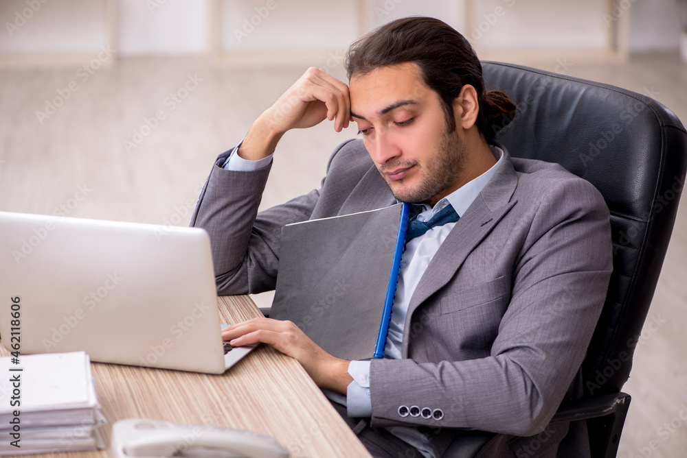 Young male employee unhappy with excessive work in the office Young male employee unhappy with excessive work in the office