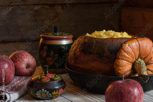 baked pumpkin with millet porridge in a cast-iron frying pan is on the table. There are apples and old wooden dishes on the table nearby.