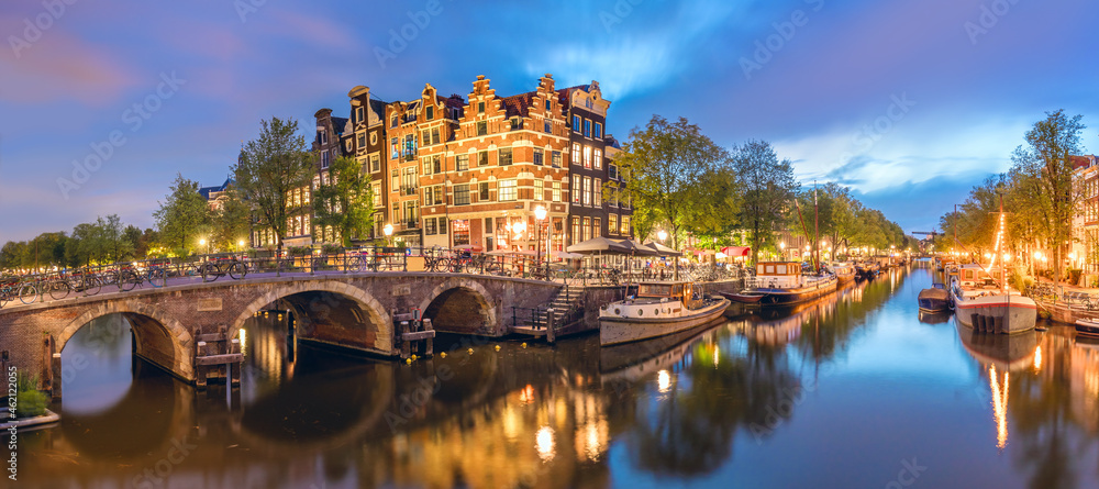 Amsterdam, Netherlands. Panorama of the historic city center of Amsterdam. Traditional houses and bridges of Amsterdam small town. A romantic evening and a bright reflection of houses in the water. 