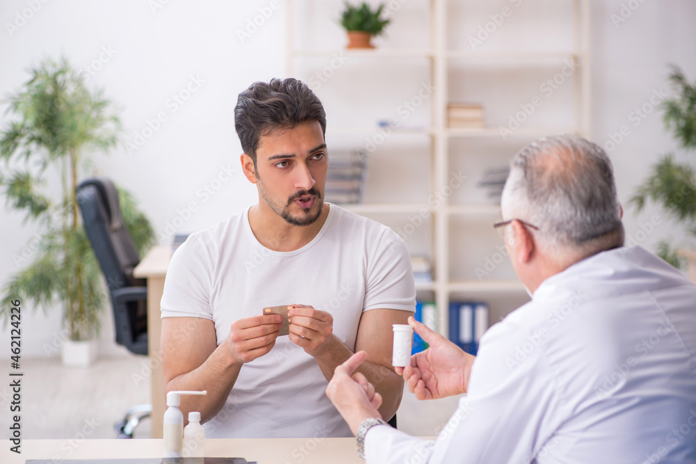 Old male doctor suggesting pills to young male patient Old male doctor suggesting pills to young male patient