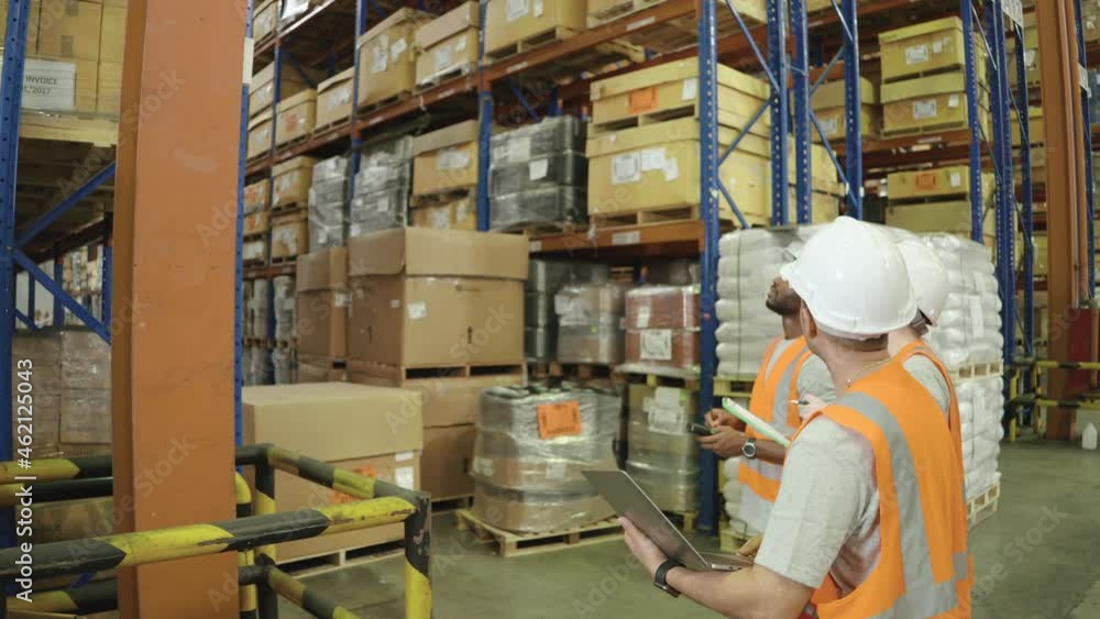 In a Logistics Center, Group of diversity workers with a safety vest and helmet wearing with a barcode scanner and laptop inspects merchandise stock in a large warehouse In a Logistics Center, Group of diversity workers with a safety vest and helmet wearing with a barcode scanner and laptop inspects merchandise stock in a large warehouse