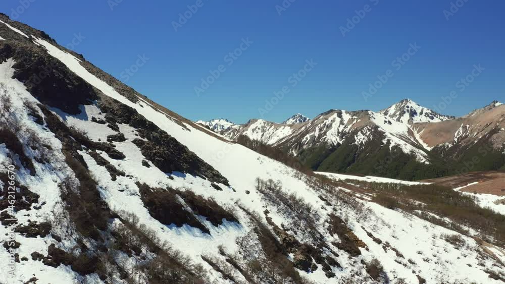 Aerial drone dolly shot of mountain side in melt in spring at the Cerro Bayo ski resort near Villa La Angostura, revealing forest and rocks on the mountains Aerial drone dolly shot of mountain side in melt in spring at the Cerro Bayo ski resort near Villa La Angostura, revealing forest and rocks on the mountains