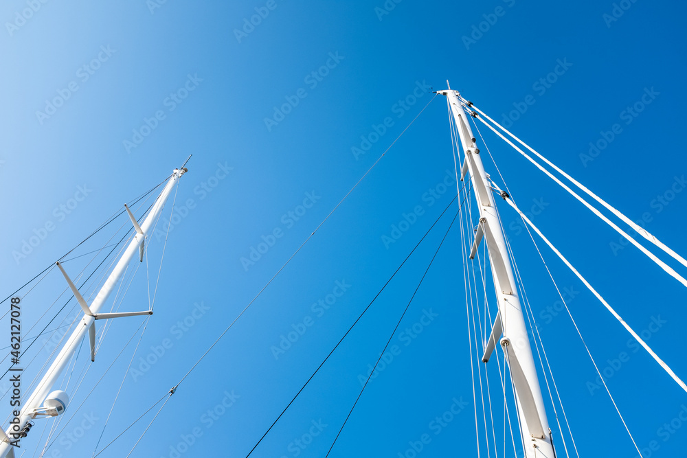 White massive masts on a sailing ship on a solid blue sky background White massive masts on a sailing ship on a solid blue sky background