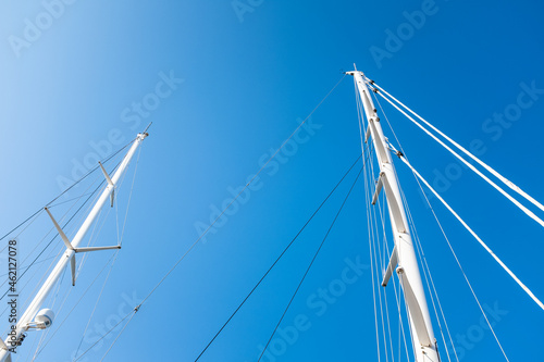 White massive masts on a sailing ship on a solid blue sky background