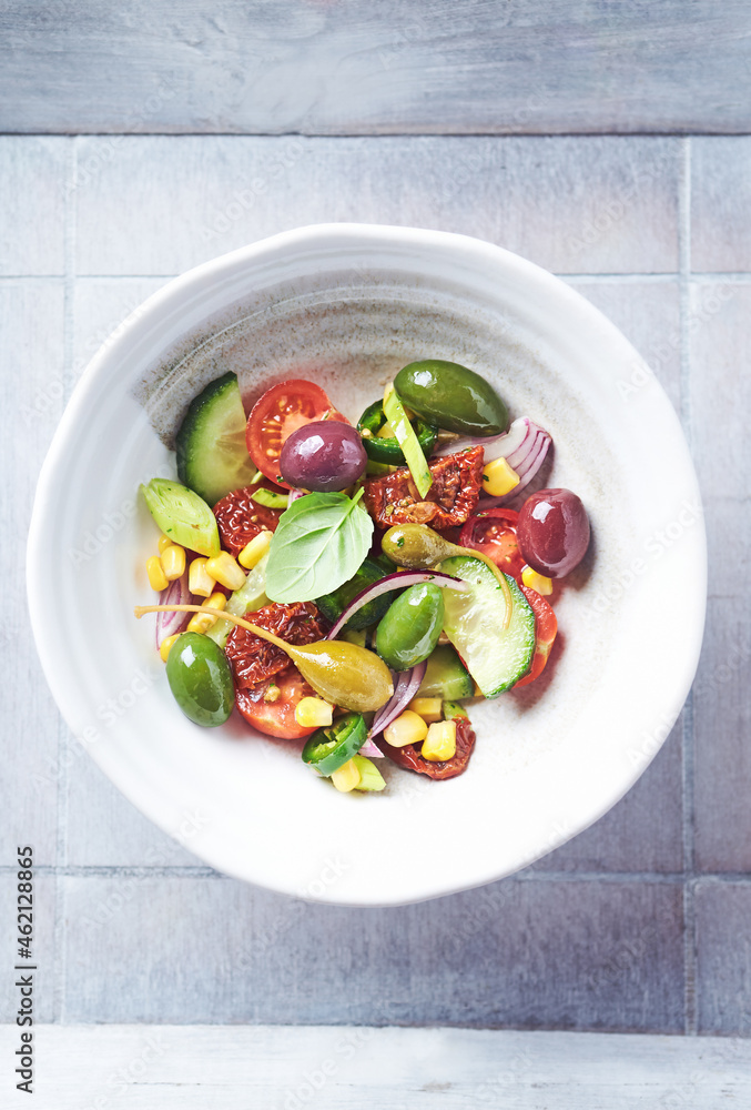 Simple Salad with Green and Kalamata Olives, Cucumber, Cherry and marinated Tomatoes, Capers and Jalapeno Pepper. Bright wooden background. Top view. Close up. Simple Salad with Green and Kalamata Olives, Cucumber, Cherry and marinated Tomatoes, Capers and Jalapeno Pepper. Bright wooden background. Top view. Close up.
