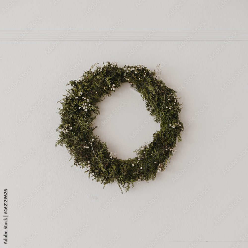 Christmas wreath made of natural fir branches hanging on a white wall. Wreath with garland lights. New Year and Christmas holidays aesthetic decoration Christmas wreath made of natural fir branches hanging on a white wall. Wreath with garland lights. New Year and Christmas holidays aesthetic decoration