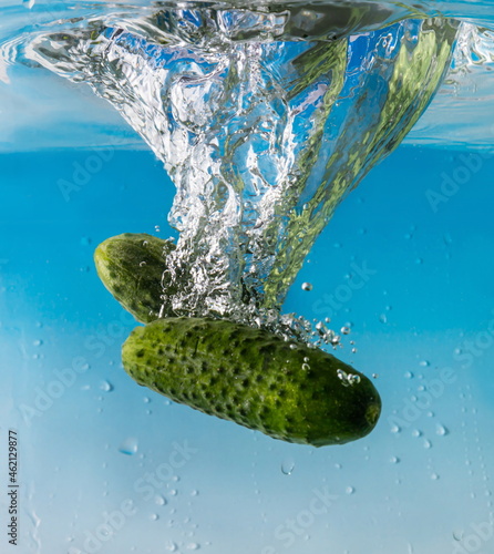 green cucumber falls into the water scattering a lot of sprays and drops