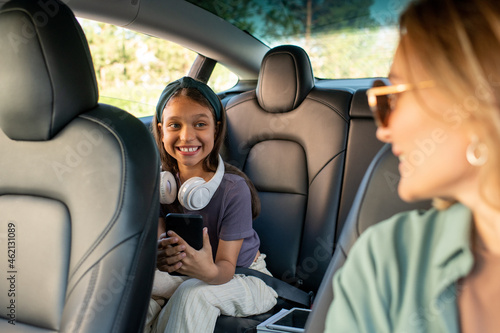 Happy daughter looking at her mom while sitting on backseat inside electric car