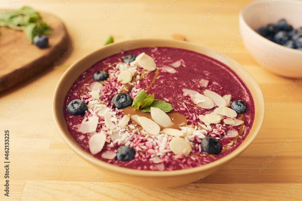 Bowl with fresh homemade smoothie decorated with blueberries, mint leaves, almond and coconut flakes Bowl with fresh homemade smoothie decorated with blueberries, mint leaves, almond and coconut flakes