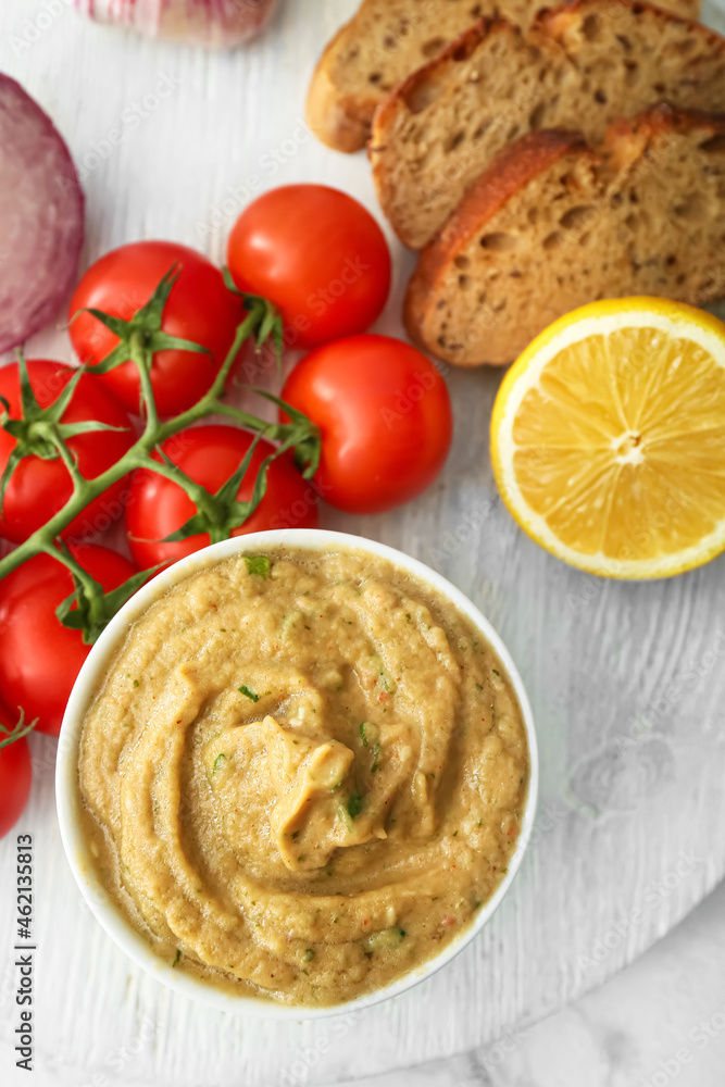 Bowl with tasty baba ghanoush, bread, lemon and tomato on light background Bowl with tasty baba ghanoush, bread, lemon and tomato on light background