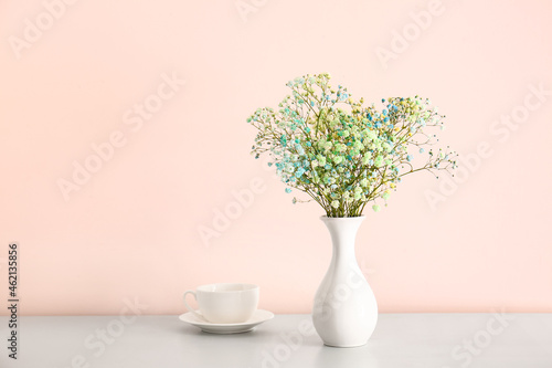 Vase with beautiful gypsophila flowers and cup on table